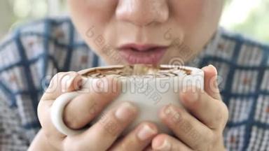 中年亚洲女人坐在咖啡馆里喝杯茶或咖啡，然后吞咽。 双手<strong>捧</strong>杯特写